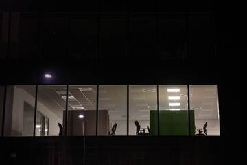 Selective blur on empty chairs and desks of an open space office seen from the Facade of a business...