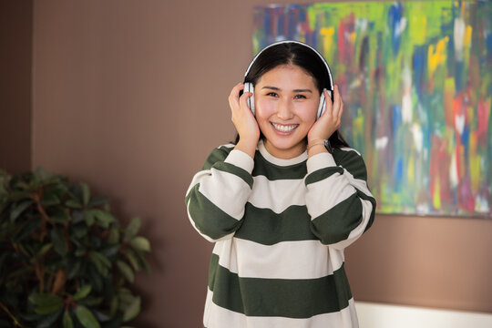 Happy kazachstan asian delighted pretty girl in casual clothes outfir wearing linkbuds headphones looking at camera smiling listening to music relaxing day off.