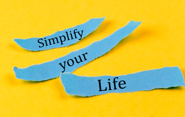 SIMPLIFY YOUR LIFE text on a blue pieces of paper on yellow background, business concept