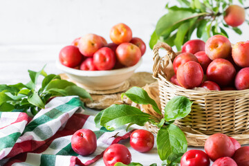 Red fresh ripe plums with water drops in wicker container on white wooden table, organic plums served for eating, healthy food and fruit  concept
