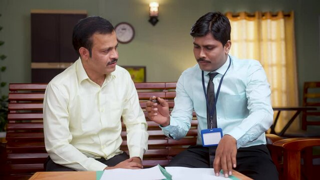 banker explaining about insurance or loan policy to middle aged man while at home - concept of financial advisor, client support and doorstep banking service