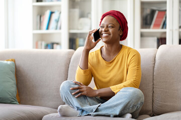 Happy black lady sitting on couch, talking on phone