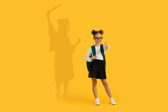 Cute Schoolgirl Showing Thumb Up, Having Shadow In Graduation Costume On Background