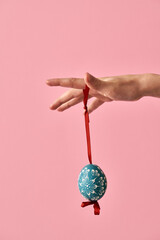 Hand holding Easter egg decorated with wax, with pink background and copy space
