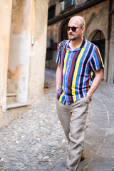 Fototapeta na wymiar A man in a colorful shirt and loose pants enjoys his vacation in the south of Italy. He strolls through the streets and has an old black camera with him. He looks relaxed and in a good mood.