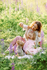 Mothers day. Young mom with daughter and small dog, hugging and  eating apples on a blanket on a picnic in a blooming lavender field. Family of two having fun, playing in meadow field