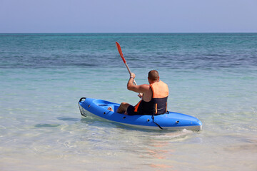 Kayaking in the sea, man wearing life vest sitting with paddle in canoe. Travel and water sports concept