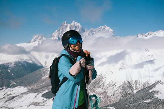 Snowboarder woman standing and smiling with snowboard beautiful mountain peaks covered with snow on background
