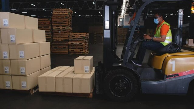 Asian male worker driving a forklift to unload or sort goods in a warehouse.