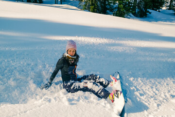 Snowboarder female fell down sitting in snow, smiling and laughing, sunny day outdoor