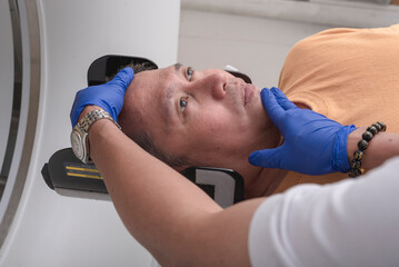Obraz premium A CT Technologist positioning the head of a male patient on a holder or cradle. Performing a head CT scan at the hospital.
