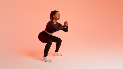 Fototapeta na wymiar Training concept. Fit african american woman doing squats exercises, working out over peach neon background, free space