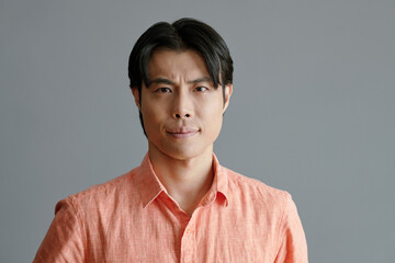 Studio portrait of young Asian man in salmon color shirt looking at camera