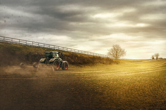 tracktor bei der ernte auf feld mit gras bein sonnenschein mit d&uuml;steren wolken
