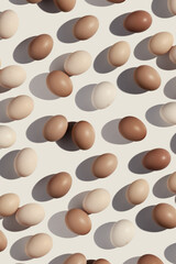 Easter eggs monochrome vertical pattern with gradient colored eggshell, hard Shadow at sunlight, beige background. Chicken eggs layout, top view, minimal flat lay, holiday food still life