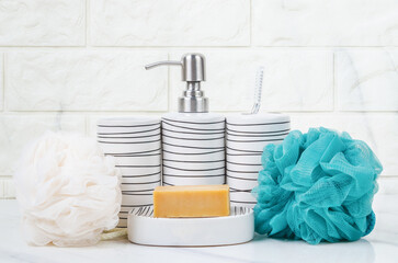 The Herb soap, shower sponge and shampoo pump bottle inside a bright bathroom background.