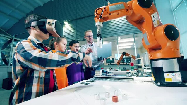 Teacher helps kids to use VR-glasses and manage robots. Virtual reality concept.