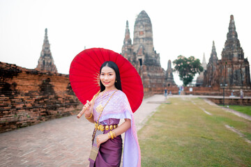 Beautiful Thai girl in traditional dress costume red umbrella as Thai temple where is the public place, Thai Woman in Traditional Costume of Thailand.