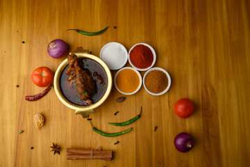 Spicy Reddish saoji Chicken Curry  Masala,with prominent Leg Piece, different spices served in brass bowl or Kadhai over  wooden background.