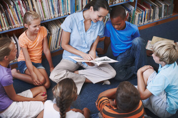 Shes such a great teacher. A pretty teacher sitting with her excited students in the library.