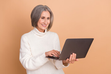 Photo of cheerful positive attractive gray bob hair elderly business woman hold laptop online meeting corporate isolated on beige color background