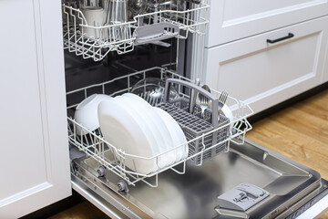 Open dishwasher with clean dishes in a white kitchen.Kitchen with integrated appliances