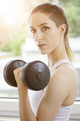 Fototapeta na wymiar Fit and strong woman building muscles with weights and dumbbell at home 