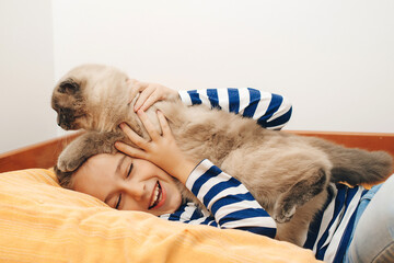 Boy relaxing on the bed with pet. Childhood, true friendship and home pet. Cute boy plays with a cat at home.