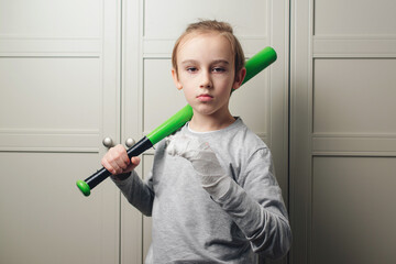 Sad boy with a broken arm in plaster holding baseball bat. Kid with broken hand after training.