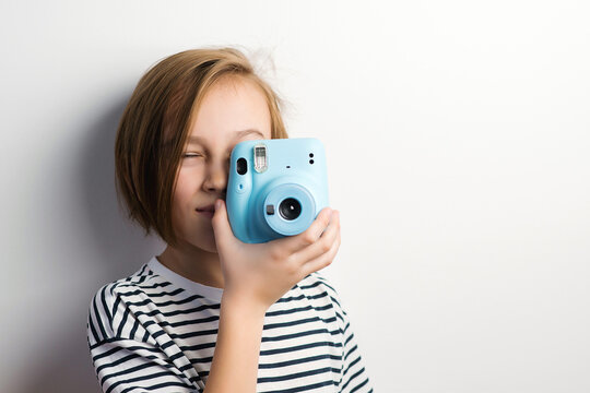 Cute boy holding photo camera. Stylish kid posing over grey background.