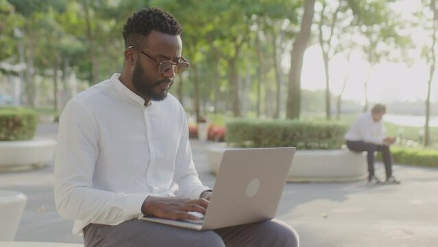 Medium shot of black businessman typing on laptop and using free Internet in city public space