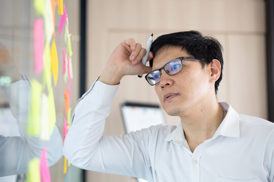 Asian office worker thoughtful about new project presentation, putting plan and idea at sticky marker on whitebord.
