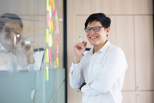 The smile on the face of the asian office worker who succeeded in the achievement business project. Standing front of whitebord that have many sticky note idea in meeting room.