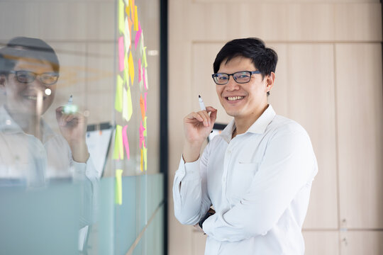 The smile on the face of the asian office worker who succeeded in the achievement business project. Standing front of whitebord that have many sticky note idea in meeting room.