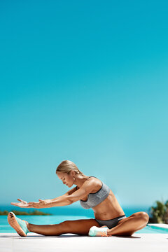 Just a little more...an attractive young woman in gym wear stretching by the pool after her workout on a sunny day.