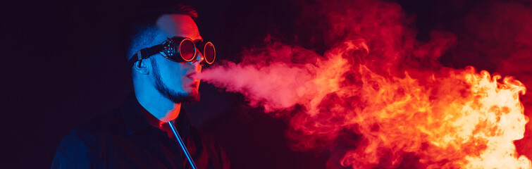 man in futuristic glasses smokes a hookah and blows a cloud of smoke in a shisha bar with red and blue neon lights