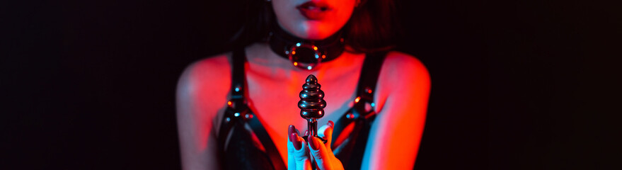metal butt plug in the hands of a slave girl with a choker and a leather belt. Panoramic wide horizontal photo for banner head cover