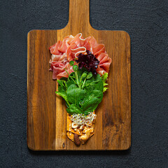 Salad of jamon (prosciutto) spinach and lettuce with crispy savory bread, nuts, microgreens on black background. Flat lay of food in form of light bulb on board. Food energy concept, top view.