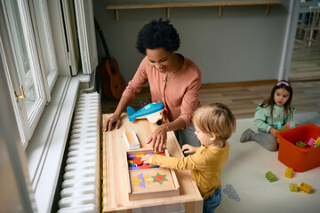 Happy African American kindergarten teacher and little boy play with puzzles.