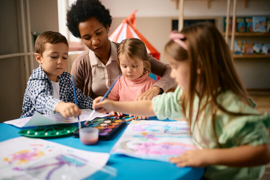 Black female teacher and group of kids coloring during art class at preschool.