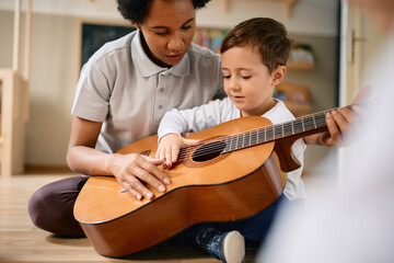 Small boy learns to play acoustic guitar with help of his African American teacher at kindergarten.