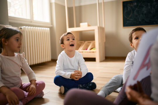 Happy little boy and his friends learn alphabet with their teacher at preschool.