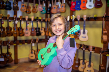 a happy child in a uklele musical instrument store, chooses a brightly colored four-string soprano