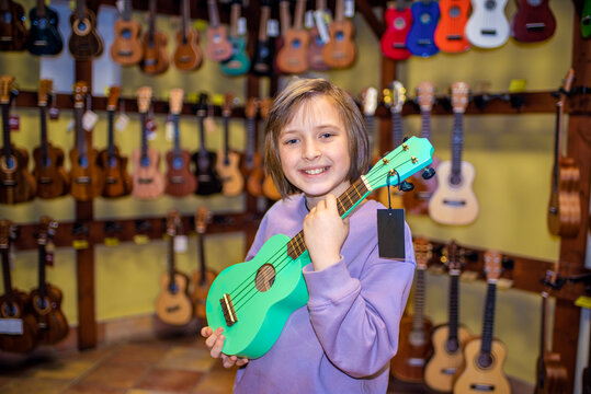 a happy child in a uklele musical instrument store, chooses a brightly colored four-string soprano - Powered by Adobe
