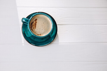 Blue mug with coffee, cappuccino on a white wooden background. Top view, close-up