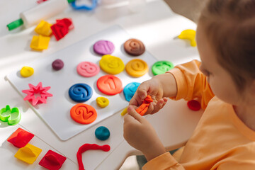 A little girl playing with colorful pieces of plasticine. Art Activity for Kids. Fine motor skills, creativity and  hobby. Sensory play for toddlers.