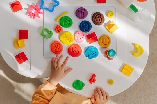 A little girl play with plasticine and creates colorful numbers.  Learning to count through play. Early education. Fine motor skills, creativity and  hobby.
