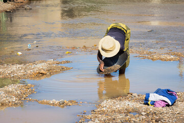 A woman panning for gold in Madagascar. Madagascar gold panner. A woman panning for gold in river. Reflection in water. 