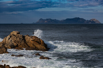 A fisherman fishes on the rocks of Baiona's coast with the Cíes Islands in the background