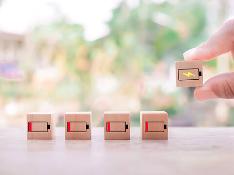 Close up hand arranging battery charging icon and wooden block with low battery icons.